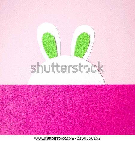 Flat lay, on a pink background rabbit hiding behind a felt background, space next to copy space for text.  Holiday concept light happy easter, children's creativity.  Close-up.  Top view, foreground.