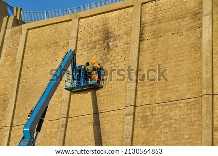 Men repair a high cliff wall on articulated arm Royalty-Free Stock Photo #2130564863
