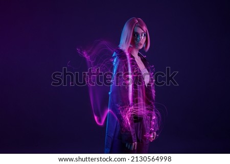 Woman in futuristic costume. Female in modern VR glasses interacting with network while having virtual reality experience. Augmented reality game, future technology, AI concept. VR. Neon purple light. Royalty-Free Stock Photo #2130564998