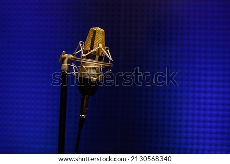 Professional microphone in a recording audio studio with acoustic panels behind it, and blue light on a background. Copy space for your text.