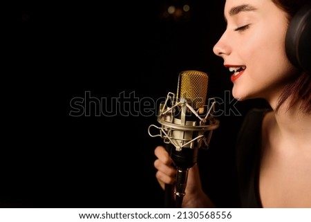 Close up of a young woman with headphones and closed eyes is recording a song in an audio recording studio on black background. Copy space for your text. 
