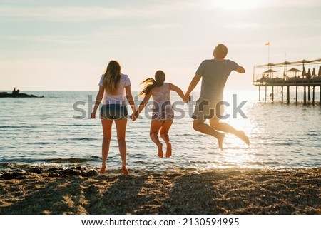 rear view. family jumping in sunlight on the shore of the sea beach. family holidays at the resort. happiness. mom, dad and daughter on vacation. the beauty of the setting sun. idyll.