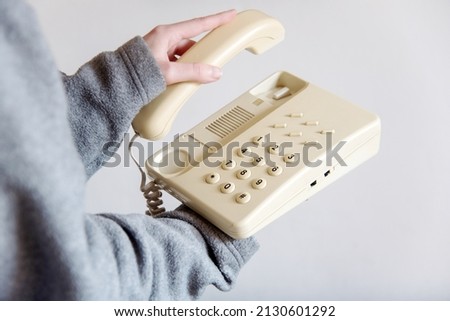 Detail of a woman's hand picking up an old white corded telephone. Hand holding the receiver of a home or office landline phone. Concept of answering a phone call. Royalty-Free Stock Photo #2130601292