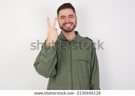 young caucasian man wearing green working overalls over white background smiling and looking friendly, showing number two or second with hand forward, counting down