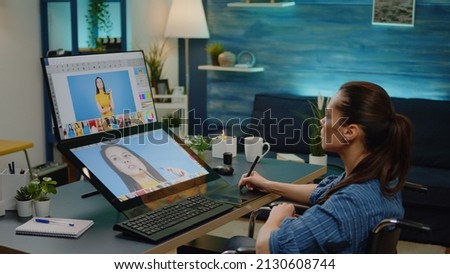Disabled editor holding stylus while doing retouch work on pictures in media studio at home. Photographer sitting in wheelchair and using editing app on touch screen for image production