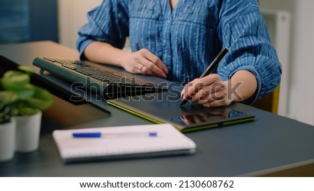 Woman photographer retouching photos with graphic tablet and stylus at photography studio. Media artist using technology on computer and retouch gadget while editing pictures in office.
