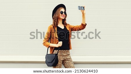 Portrait of stylish happy smiling young woman taking selfie by smartphone on gray background