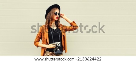 Portrait of stylish young woman photographer with film camera on gray background
