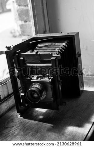 A vertical grayscale shot of a vintage camera on a windowsill 
