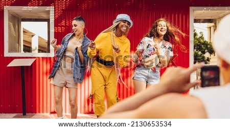 Energetic female friends dancing in front of a camera phone outdoors. Group of generation z friends having fun together in the city. Vibrant young people creating content for their social media vlog. Royalty-Free Stock Photo #2130653534
