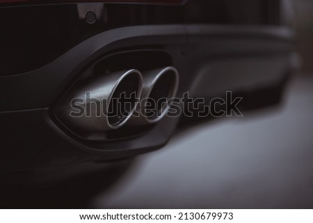 Double oval exhaust tips on a modern sport car or SUV. Visible two tailpipes coming out from an opening in the rear bumper. Black color. Royalty-Free Stock Photo #2130679973