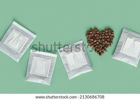 Drip coffee bag and heart from coffee beans, ground coffee for brewing in cup, pack with paper bag drip coffee filter, mint color background, top view, minimal flat lay with copyspace, pastel color Royalty-Free Stock Photo #2130686708