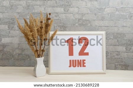 june 12. 12th day of month, calendar date.  White vase with ikebana and photo frame with numbers on desktop, opposite brick wall. Concept of day of year, time planner, summer month.