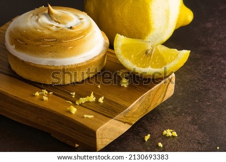 Close-up of a delicious handmade French meringue lemon tart on wooden board and dark background.