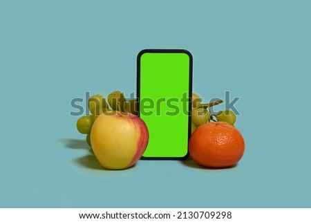 Online shopping. A smartphone with a green screen, mandarine, apple and grapes on a blue background. Mock up