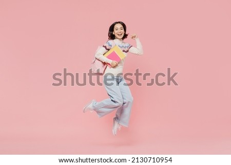 Full length happy teen student girl of Asian ethnicity wearing sweater hold backpack books jump high do winner gesture isolated on pastel plain pink background Education in university college concept Royalty-Free Stock Photo #2130710954