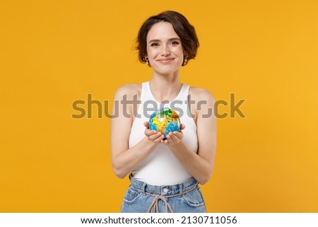 Young smiling caucasian geography student teacher woman 20s wearing white tank top shirt hold in palms Earth world globe isolated on yellow color background studio portrait. People lifestyle concept Royalty-Free Stock Photo #2130711056