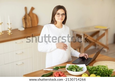 Portrait of a pregnant woman in the kitchen with a laptop on the table. High quality photo