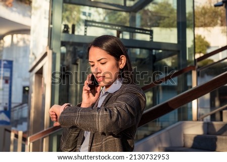 Young business woman looking the clock while talk on the phone. Royalty-Free Stock Photo #2130732953