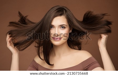 Hair Beauty Model. Brunette Woman with Straight Hairstyle flying on Wind over Dark Beige. Young Smiling Girl with Smooth Skin Make up Royalty-Free Stock Photo #2130735668