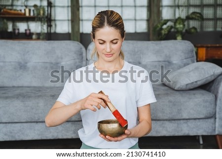 A cute girl holds a Tibetan singing bowl in her hands. Therapeutic sound of high frequencies and vibrations from bowls. Meditating girl. High quality photo Royalty-Free Stock Photo #2130741410