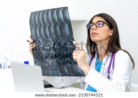 A young dark-haired female doctor with glasses examines an MRI scan in a medical office.Medical concept. Royalty-Free Stock Photo #2130744521