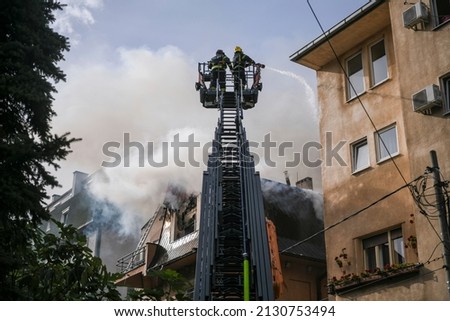 Dramatic scene of Firefighters rising on a mechanical sliding ladder crane to the epicenter of the fire. Boom crane with firefighters using extinguishing water. Translation: "Firefighters"