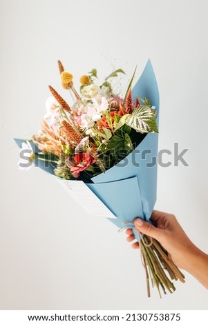Stylish minimalist bouquet of wildflowers wrapped in paper in the hands of a florist. Beautiful pattern with neutral colors, copy space.  Royalty-Free Stock Photo #2130753875