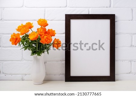Black brown  frame mockup with globeflowers in the white vase. Empty frame mock up for presentation design. Template framing for modern art.