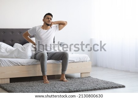 Uncomfortable Bed. Arab Man Waking Up With Neck And Back Pain, Young Middle Eastern Male Suffering Backache While Sitting In Bedroom At Home, Frowning And Massaging Aching Zones, Copy Space Royalty-Free Stock Photo #2130800630
