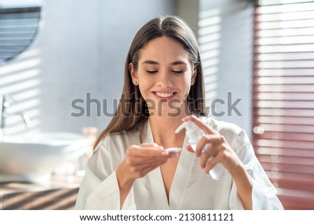 Happy young lady applying hydrophilic oil on cotton pad for cleansing face, smiling beautiful woman making daily skincare routine in bathroom, enjoying making beauty treatments at home, free space Royalty-Free Stock Photo #2130811121