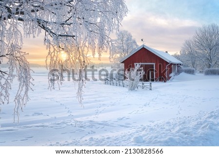 Winter view of a red barn at sunset in Rusko, Finland. Trees covered with snow. Royalty-Free Stock Photo #2130828566