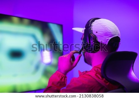 Rear view young Player video computer pc. Young man sitting on chair in game station.Streamer man wearing headphone  playing action game online in the darkroom.