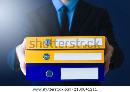 Office man in suit and tie in with stack of ring binders for archiving documents over clean background. File, Ring Binder, Emotional Stress. Royalty-Free Stock Photo #2130841211