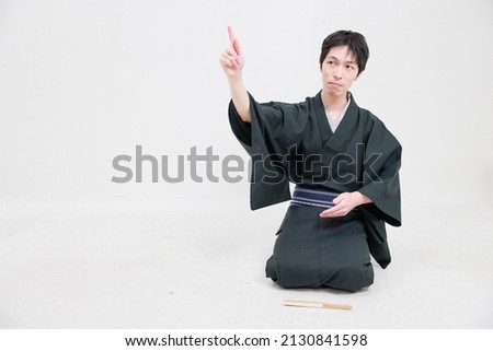 A man in a kimono sits upright and points to a space