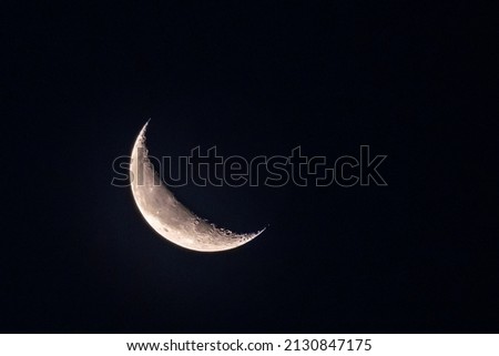 Crescent Moon with visible craters, mountains and lunar mare on Clear Sky at Night