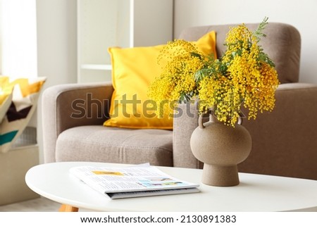 Vase with mimosa flowers and magazine on table in living room Royalty-Free Stock Photo #2130891383