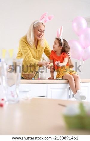 Happy little girl and her grandmother with bunny ears and Easter eggs at home