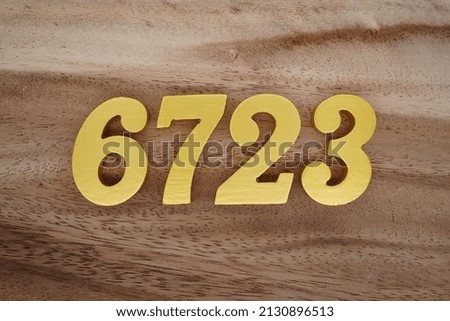Wooden  numerals 6723 painted in gold on a dark brown and white patterned plank background.
