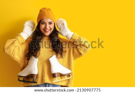 Pretty young woman in winter clothes and with ice skates on color background