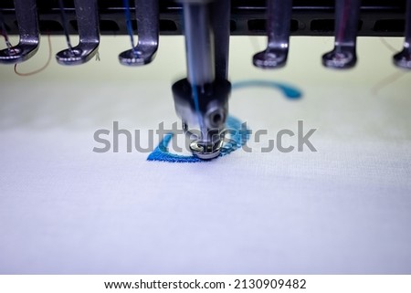 Machine embroidery of the letter "S" on a cotton cloth with blue thread. Blurred photo up close.