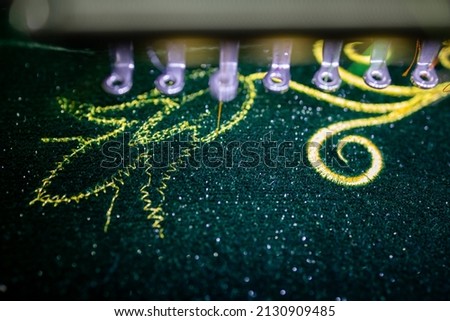 Machine embroidery of flowers with golden thread on green velvet fabric.