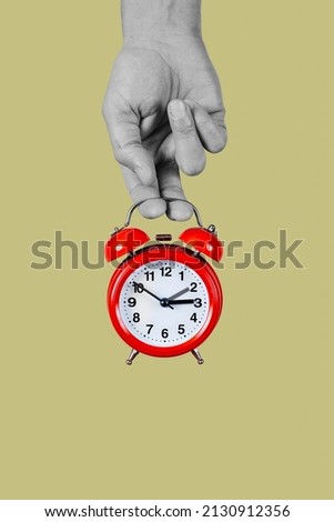 a man holds in his hand, in black and white, a classic red alarm clock, that is setting one hour backwards or forwards, at the beginning or the end of the summer time Royalty-Free Stock Photo #2130912356