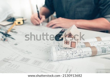 Mini model house on roll blueprint plan and architector use pen drawing on blueprint background. House Architect design and engineer concept.