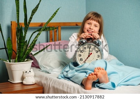 Child girl woke up in a good mood, holding alarm clock. I slept well, it's time to get up and good morning. Healthy sleep. Royalty-Free Stock Photo #2130917882