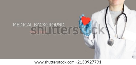 Big medical banner with text. A doctor on a gray background in a white coat holds a red wooden heart in his hands. The concept of health, care, kindness. Gray banner with copy space.