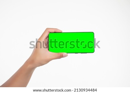Image of hand holding a phone with a green screen in landscape orientation. on a white background. Royalty-Free Stock Photo #2130934484