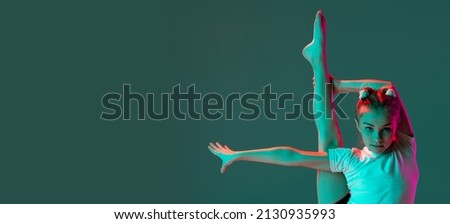 Little flexible girl, rhythmic gymnastics artist training isolated on green studio background in neon pink light. Doing exercises in flexibility. Beauty, sport, challenges, studying, ad