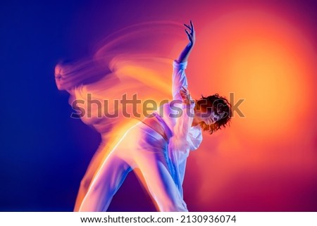 Sport and beauty. Image of flexible young girl, hip-hop dancer in white outfit dancing hip hop isolated on blue background in yellow neon light. Youth culture, hip-hop, movement, style and fashion Royalty-Free Stock Photo #2130936074
