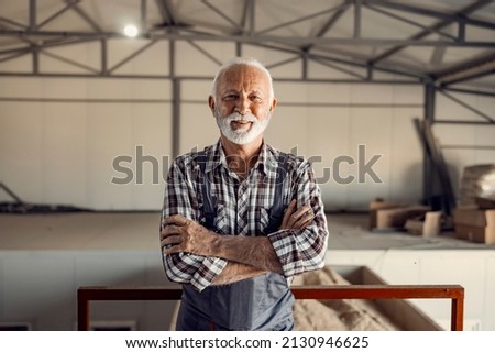 Successful senior factory workers. A proud successful smiling senior factory worker in working uniform is standing in the factory with arms crossed. Royalty-Free Stock Photo #2130946625